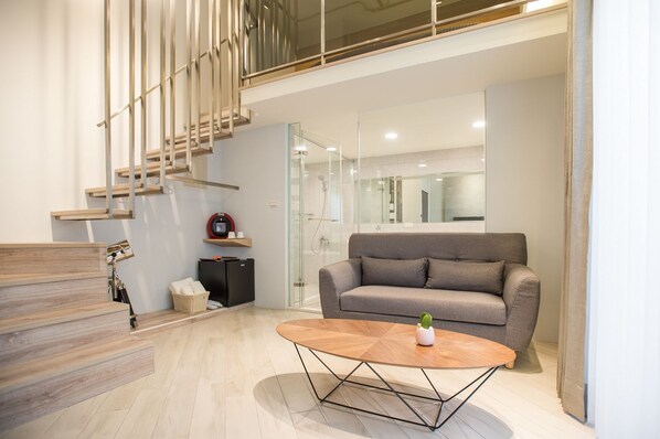 Una sala de estar moderna con un sofá gris, una mesa de centro de madera y una escalera de diseño minimalista.