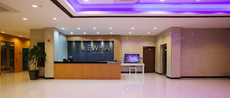 A hotel reception area with a modern design, including a reception desk, a television, and a potted plant.