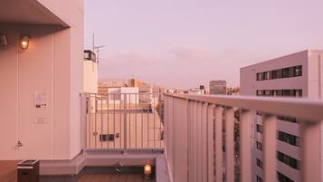 A balcony with a view of adjacent buildings, a metal railing, and a wooden floor.