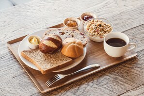 Bandeja de desayuno con pan, mantequilla, mermelada, nueces y café sobre una mesa de madera.