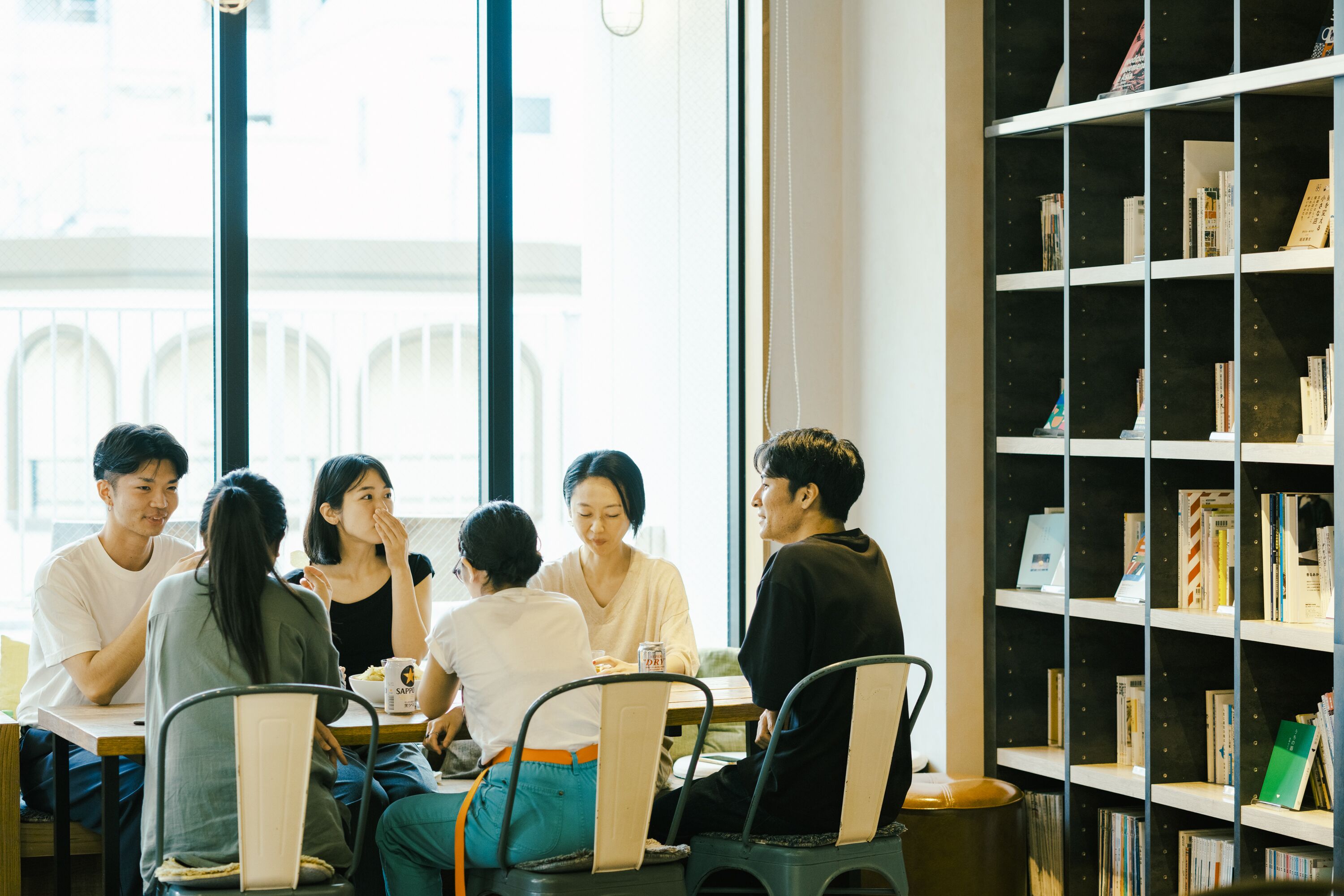 A group of people sitting around a table in a cafe with a bookshelf in the background.