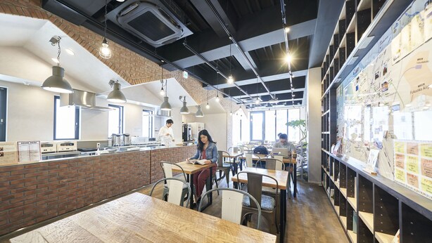 A modern cafe with brick walls, wooden tables, and hanging pendant lights. - WeBase Hakata Hostel (Fukuoka)