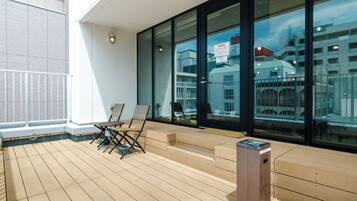 A deck with a wooden floor, a small table with chairs, and a trash bin.