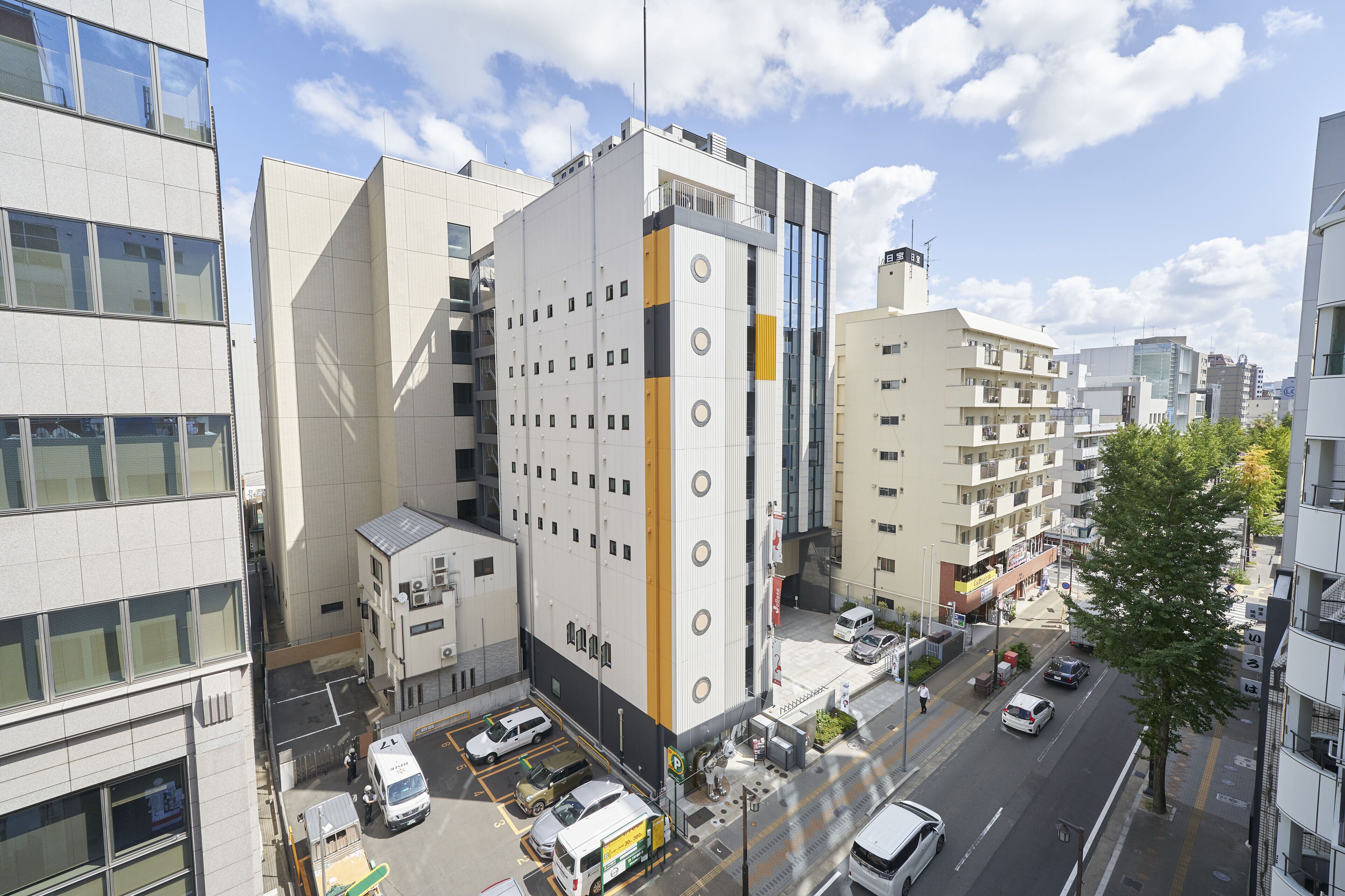 A multi-story building with a modern architectural design, featuring a mix of glass and concrete facades, and a parking area with several vehicles.