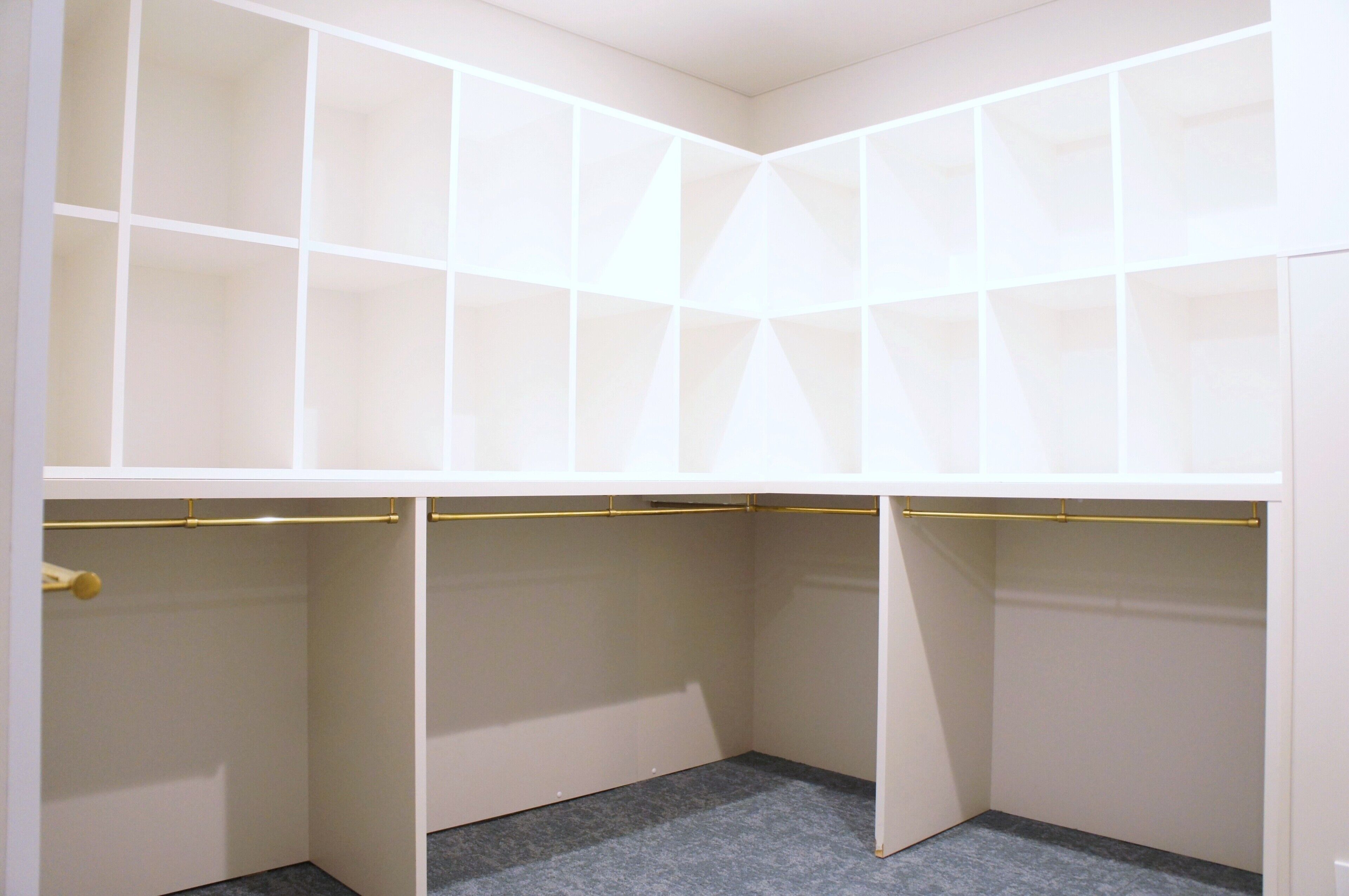 A corner closet with multiple compartments and a gold-colored rod.