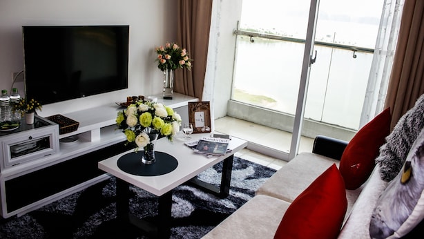 A living room with a flat-screen TV, a coffee table with a vase of flowers, a sofa with red cushions, and a view of a balcony. - Maxshare Hotels & Serviced Apartments (Bai Chay)
