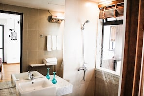 A bathroom with a sink, two glass vases, a towel rack with towels, a shower with a handheld showerhead, and a window with blinds. - Maxshare Hotels & Serviced Apartments (Bai Chay)