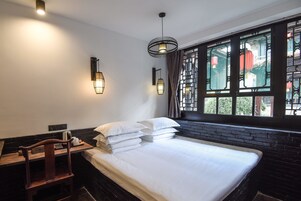 A hotel room with a bed, a desk with a chair, and a window with decorative elements.