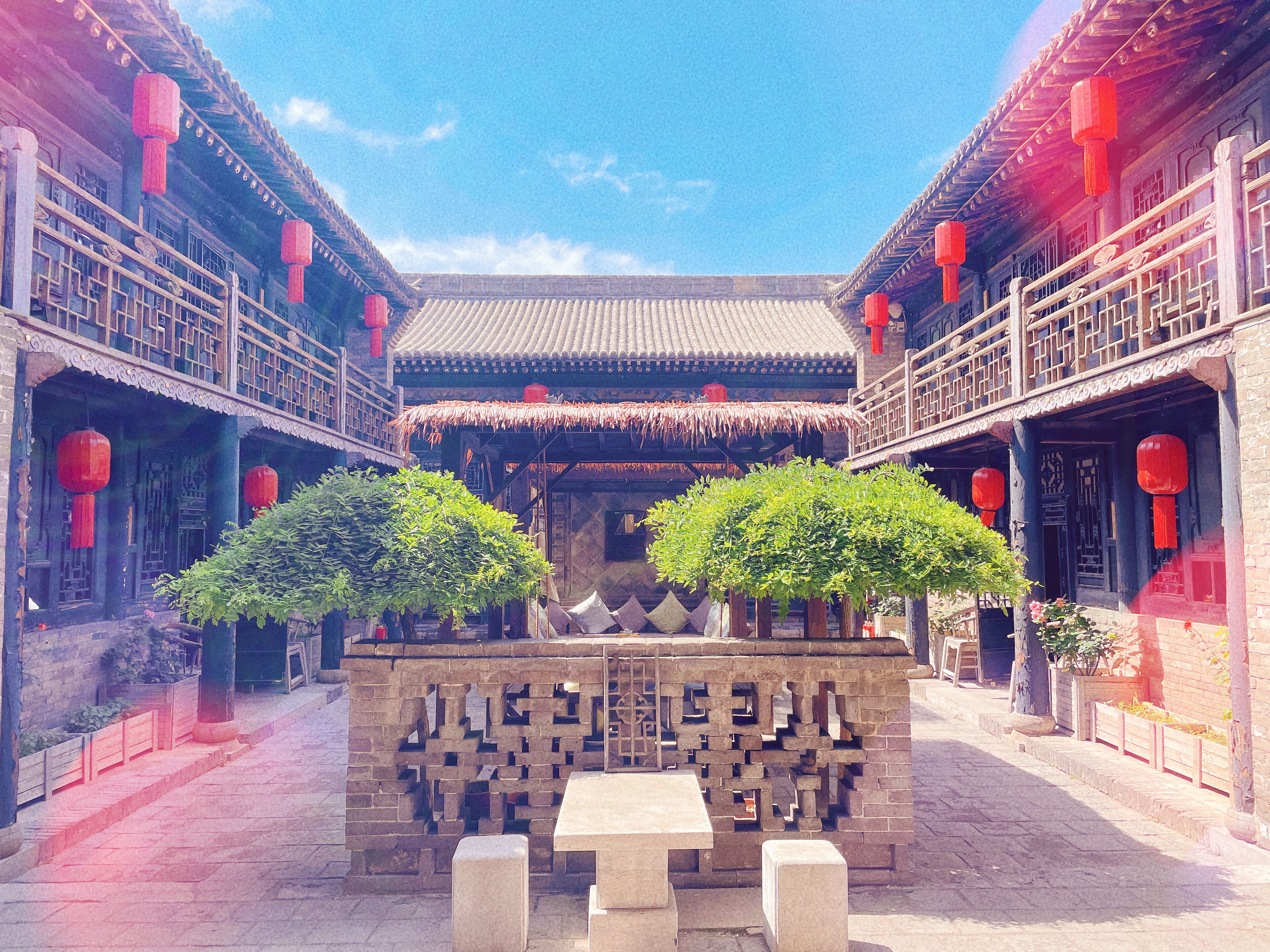 A courtyard with traditional architecture, featuring a central stone structure and red lanterns.