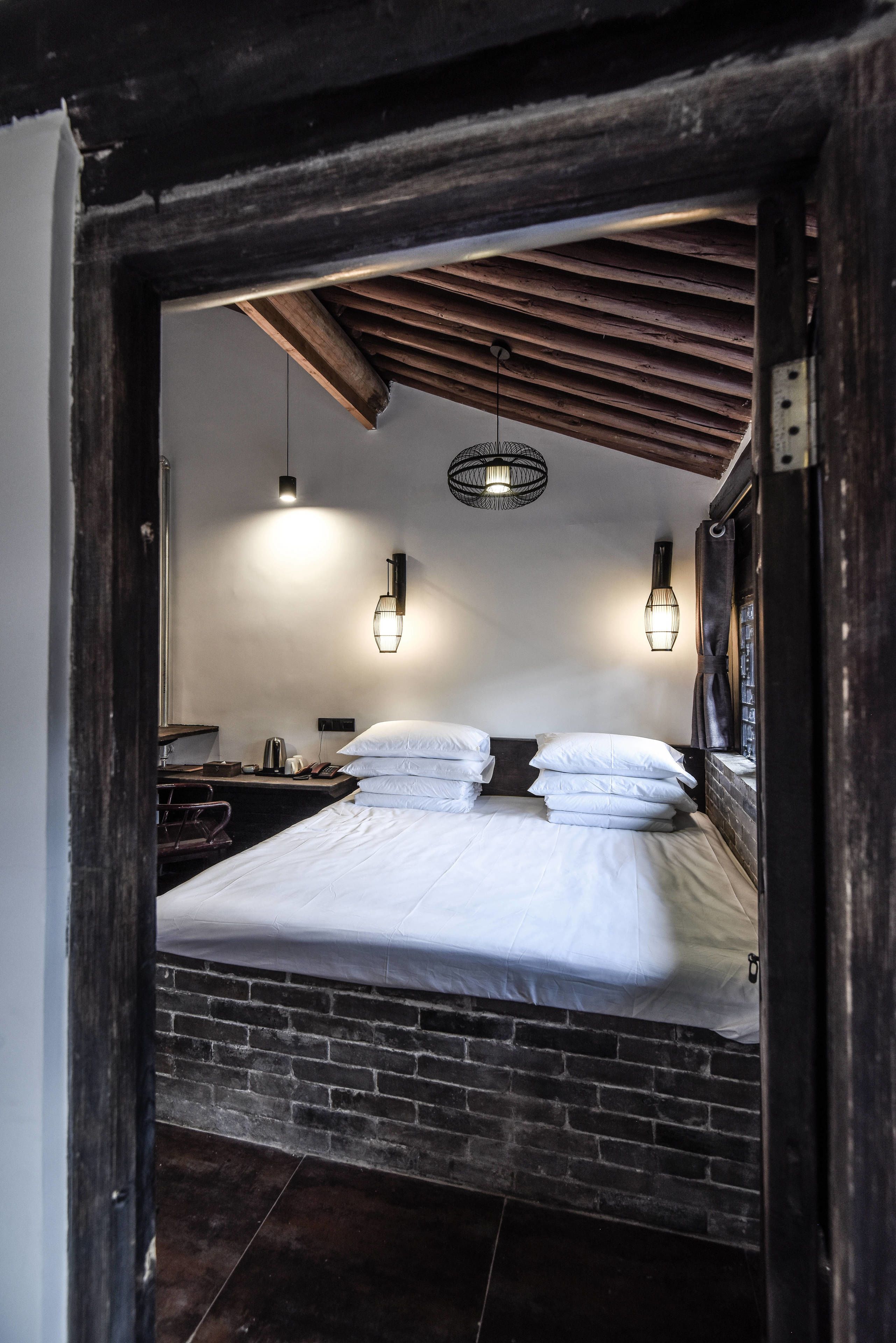 Una habitación con una cama, dos luces empotradas, una lámpara colgante y una pared de ladrillo.