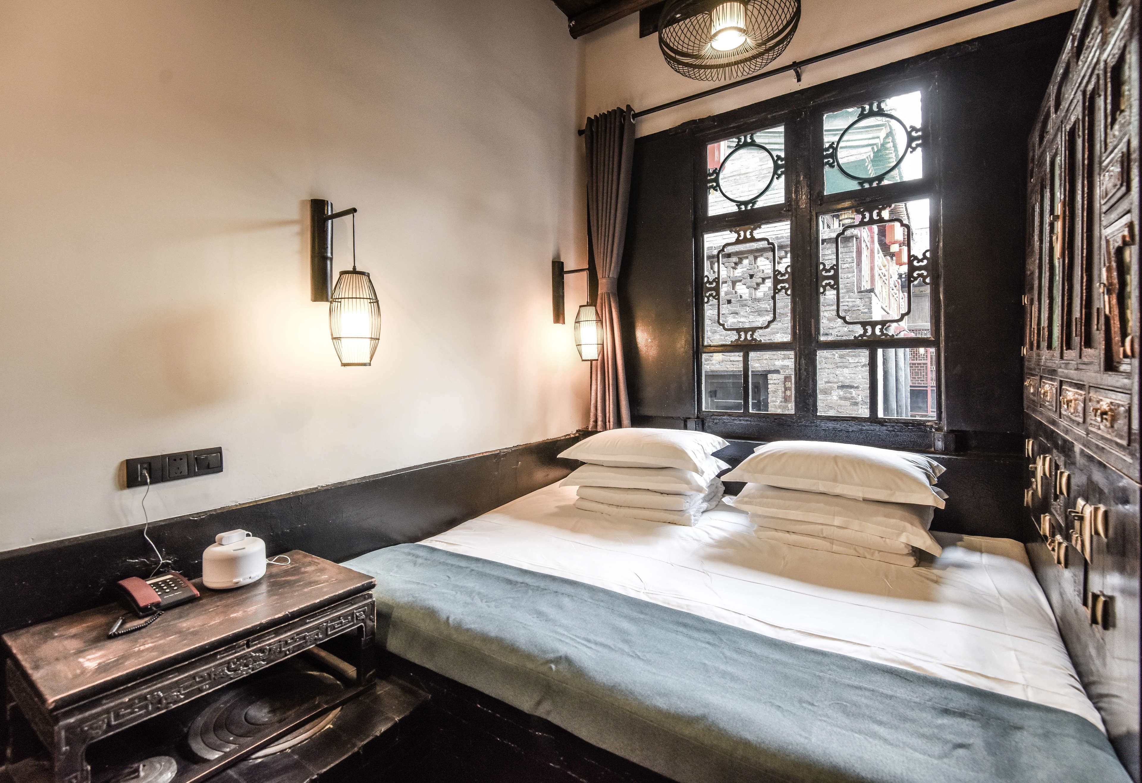 Een klassieke kamer met een bed, een klein tafeltje met een telefoon en waterkoker, en een raam met decoratieve glas-in-loodramen.