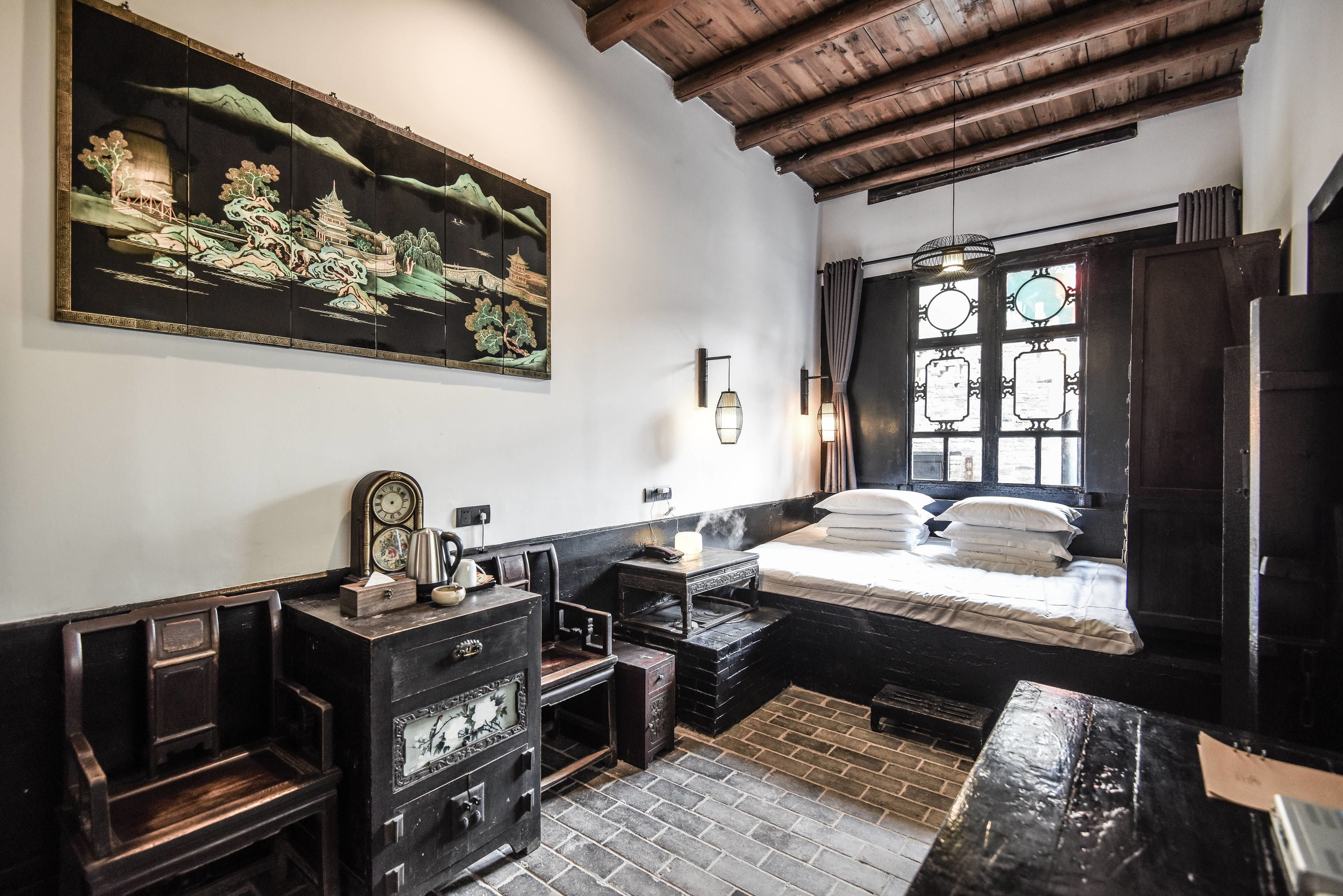 A traditional room with a bed, a wooden bench, a dresser, and a large painting on the wall.