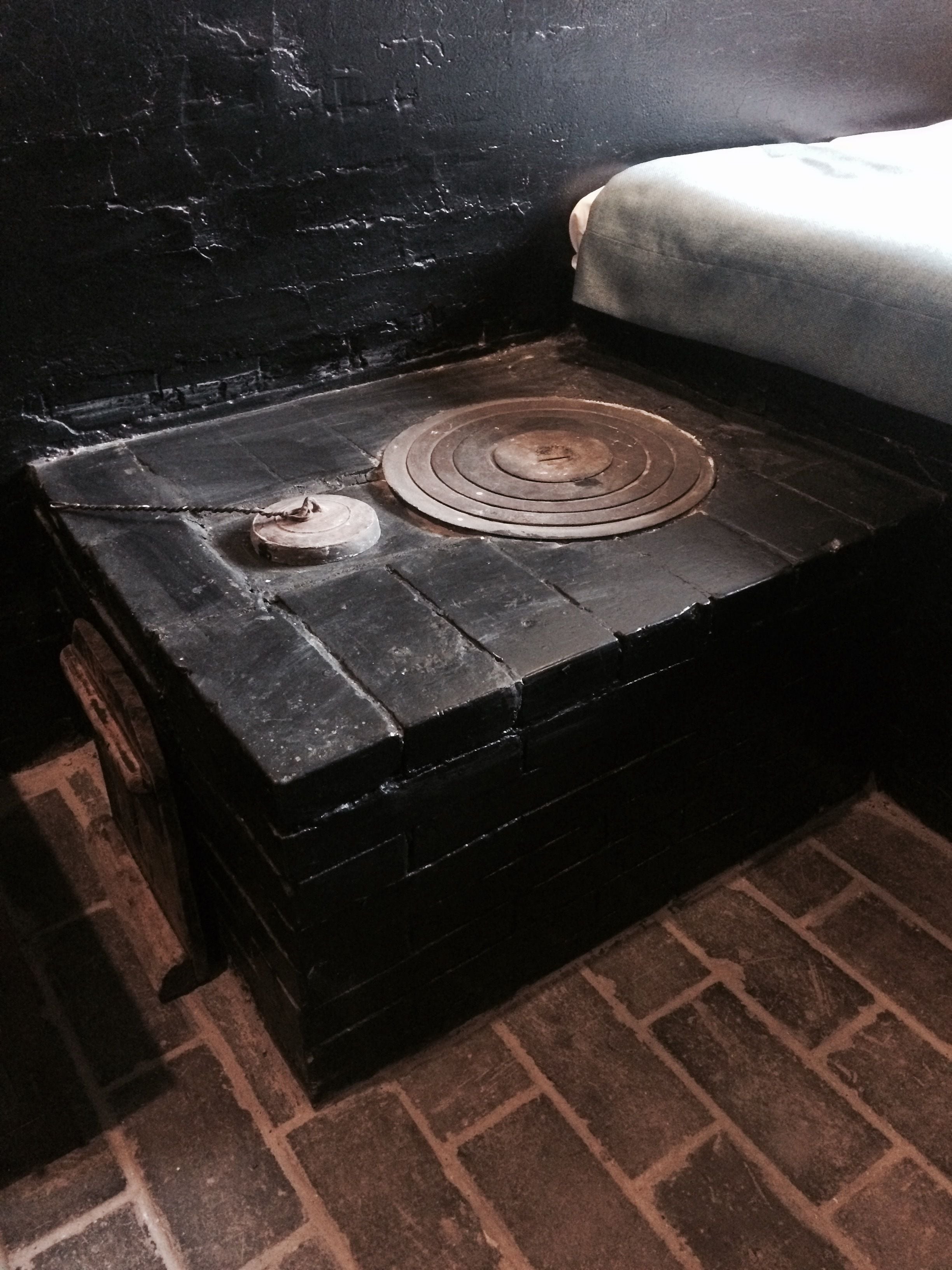 A small, dark wooden chest with a circular metal object on top, placed on a brick floor next to a black wall.
