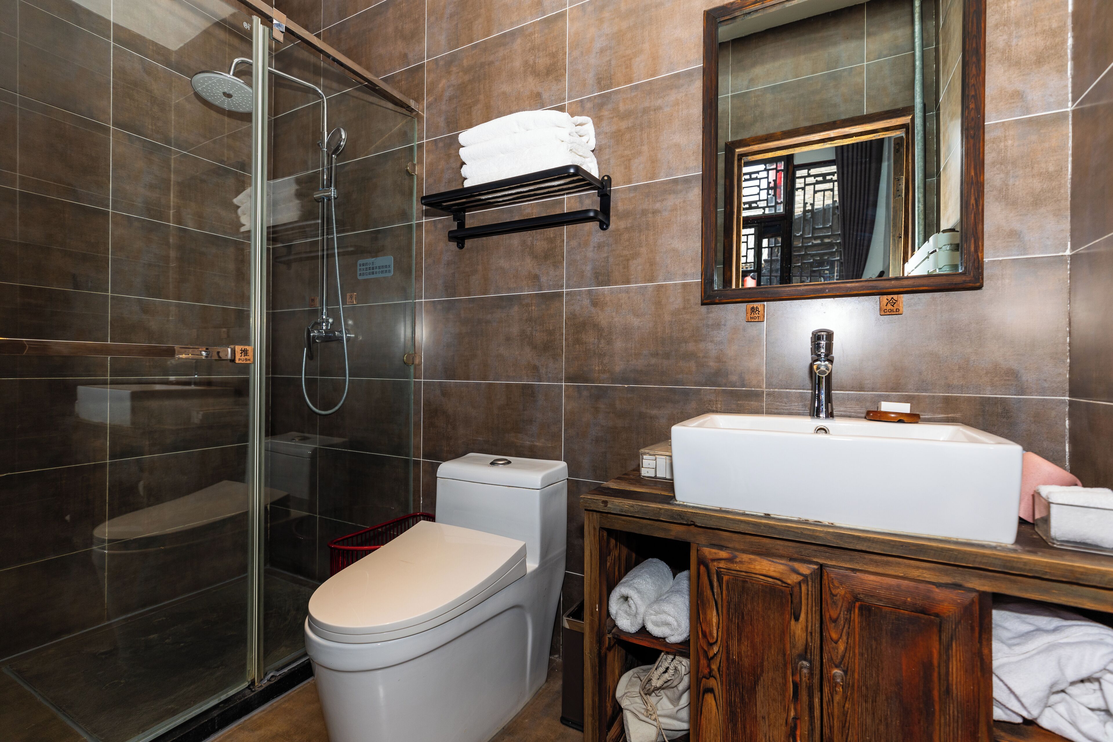 A modern bathroom with a glass-enclosed shower, a white toilet, a wooden vanity with a sink, and a mirror above the vanity.