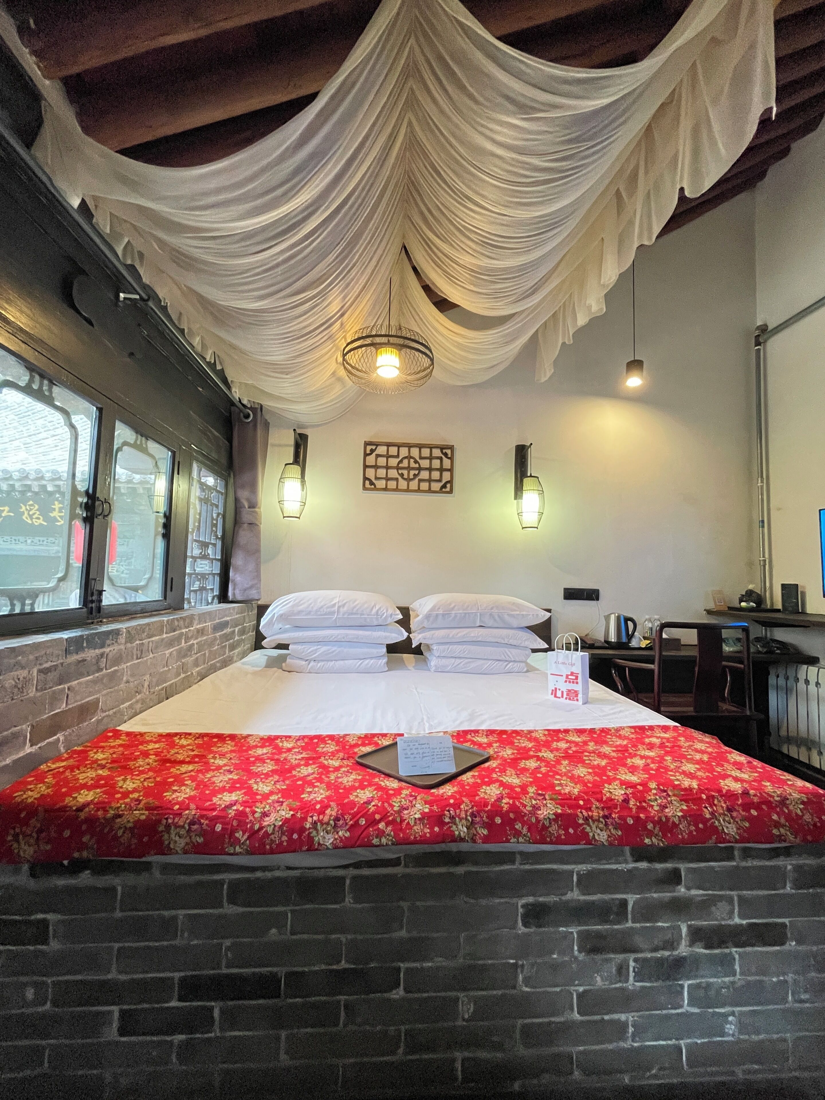 A hotel room with a bed, a brick wall, a window, and a hanging light fixture.