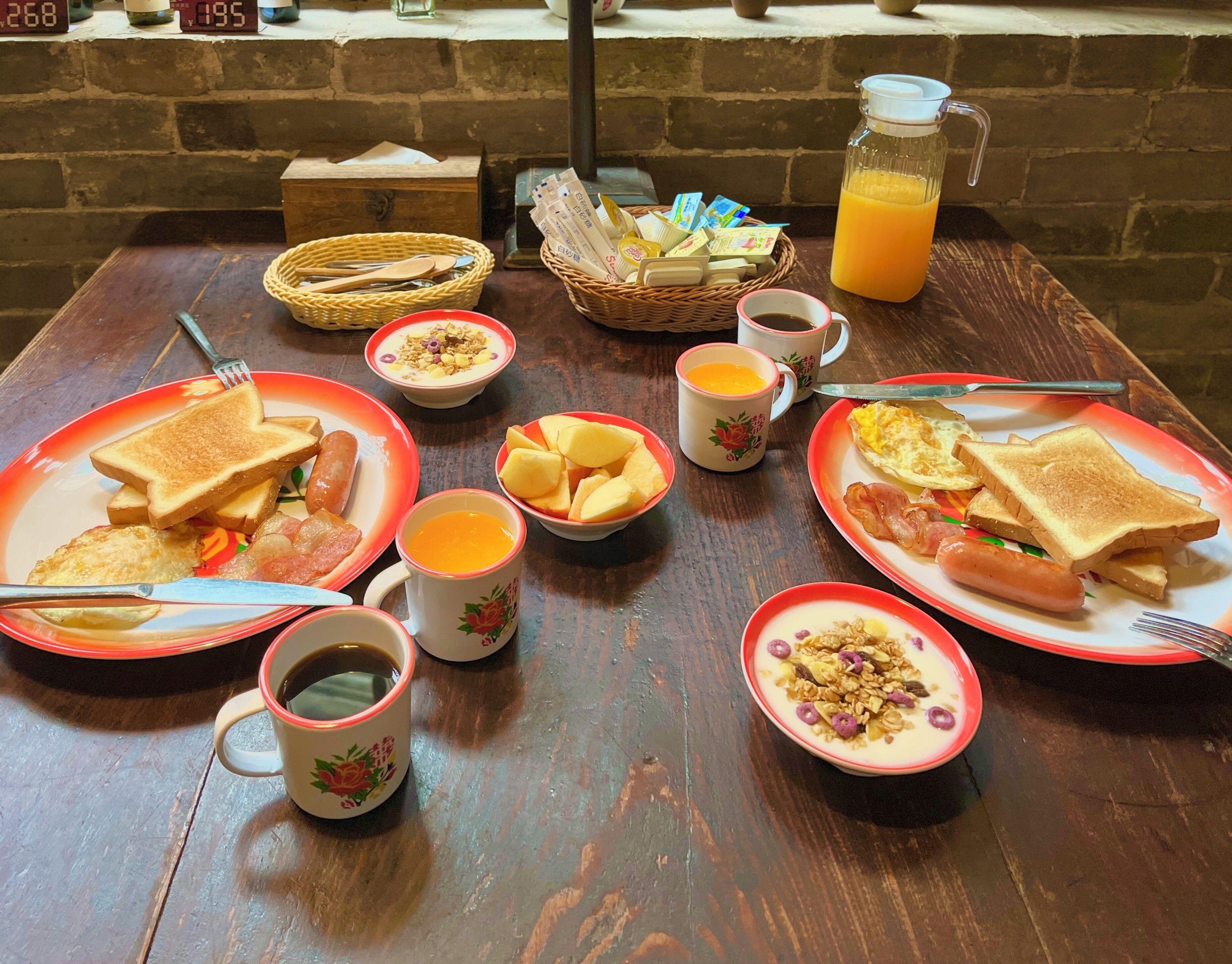 Et morgenbord med toast, pølser, æg og frugt, samt kopper med kaffe og juice.