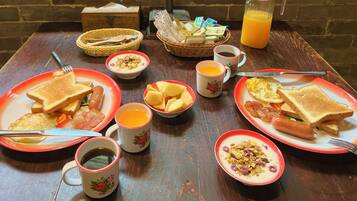 Et morgenbord med toast, pølser, æg og frugt, samt kopper med kaffe og juice.