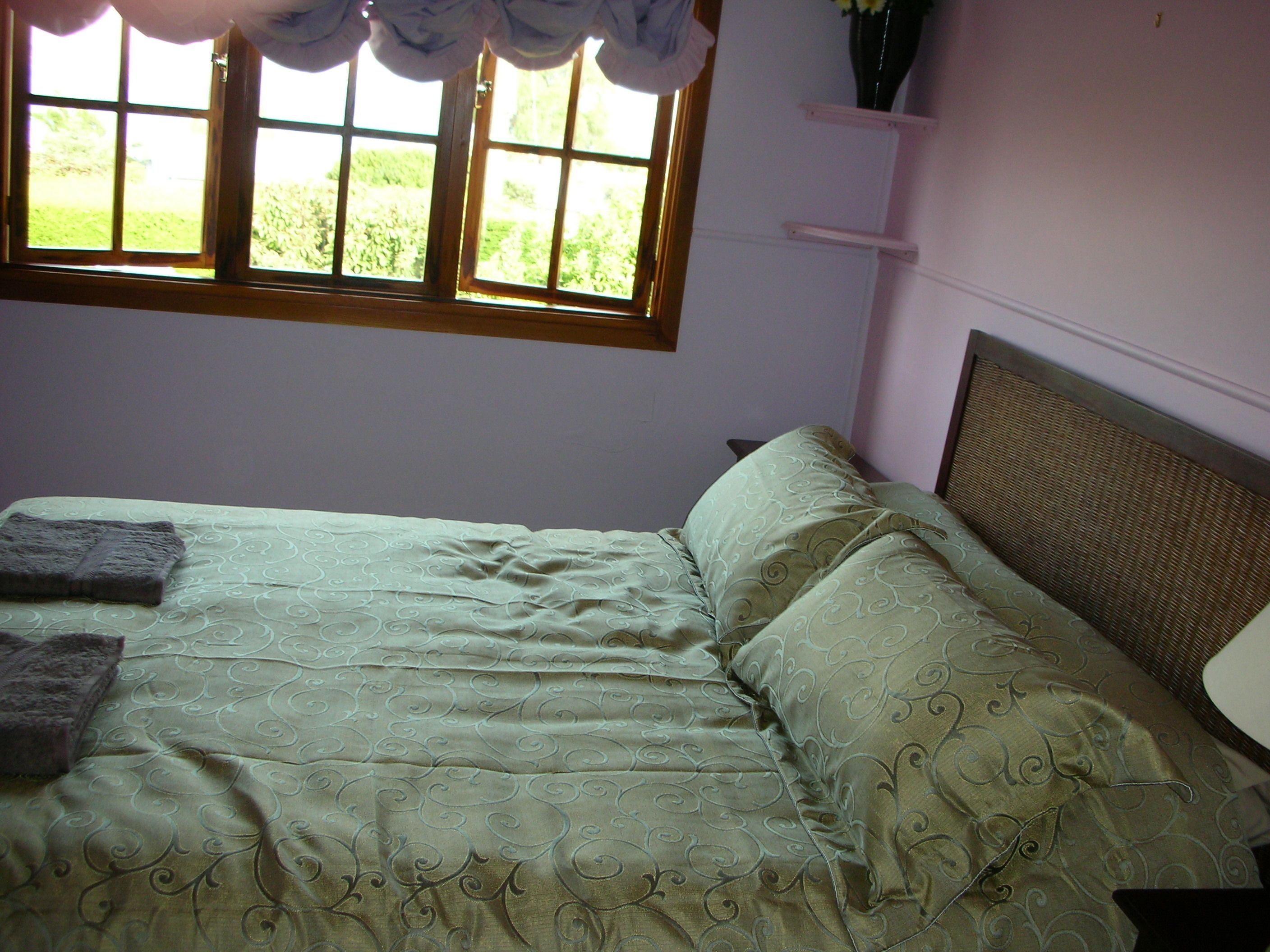 Une chambre à coucher avec un lit, une fenêtre avec des rideaux, une table de chevet et une étagère fixée au mur.