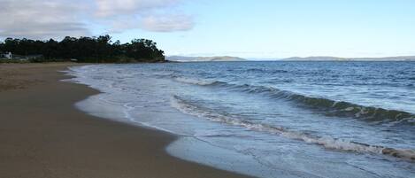 A beach with gentle waves, a clear sky, and distant mountains.