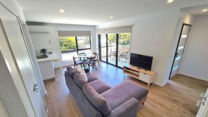 Ein modernes Wohnzimmer mit grauem Sofa, Fernseher und einem Essbereich mit Tisch und Stühlen.