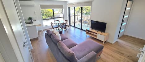 A modern living room with a grey sofa, a TV, and a dining area with a table and chairs.