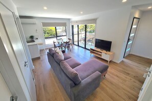 Un salon moderne avec un canapé gris, un téléviseur et un coin repas comprenant une table et des chaises.