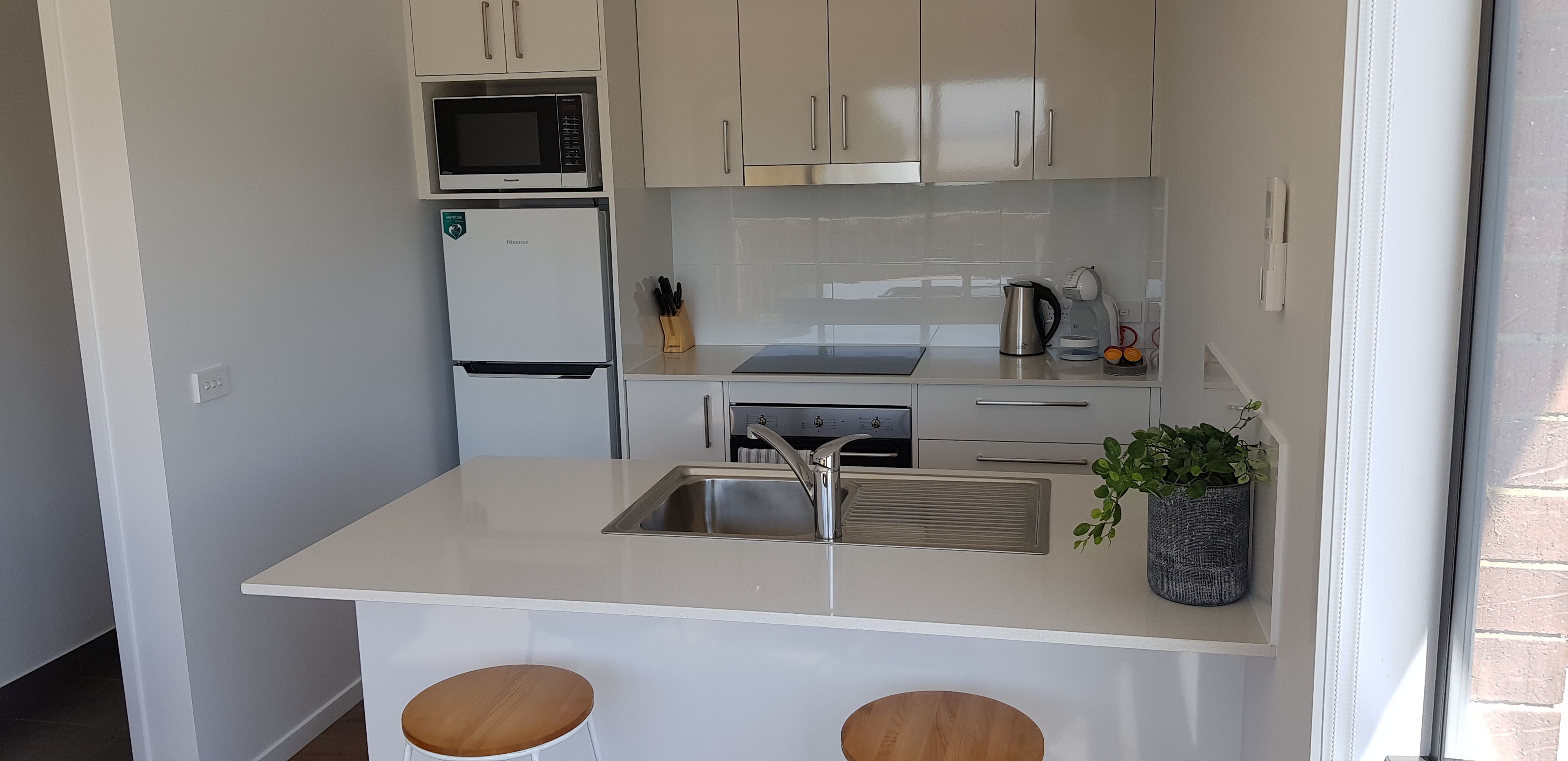A compact kitchen with a microwave, refrigerator, sink, and a small bar area with stools.
