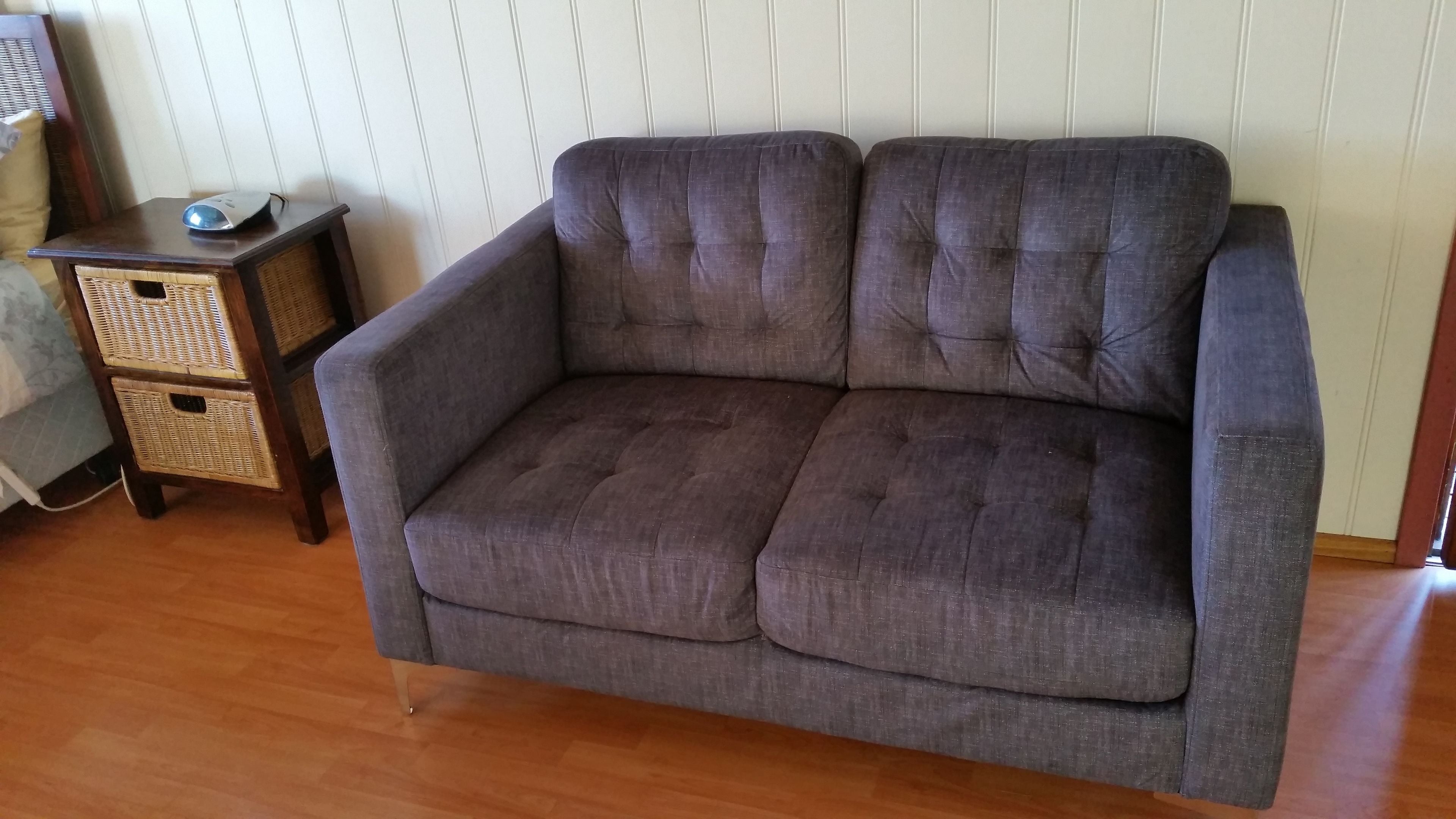 Un sofá gris con base de madera y una mesita auxiliar con un ratón.
