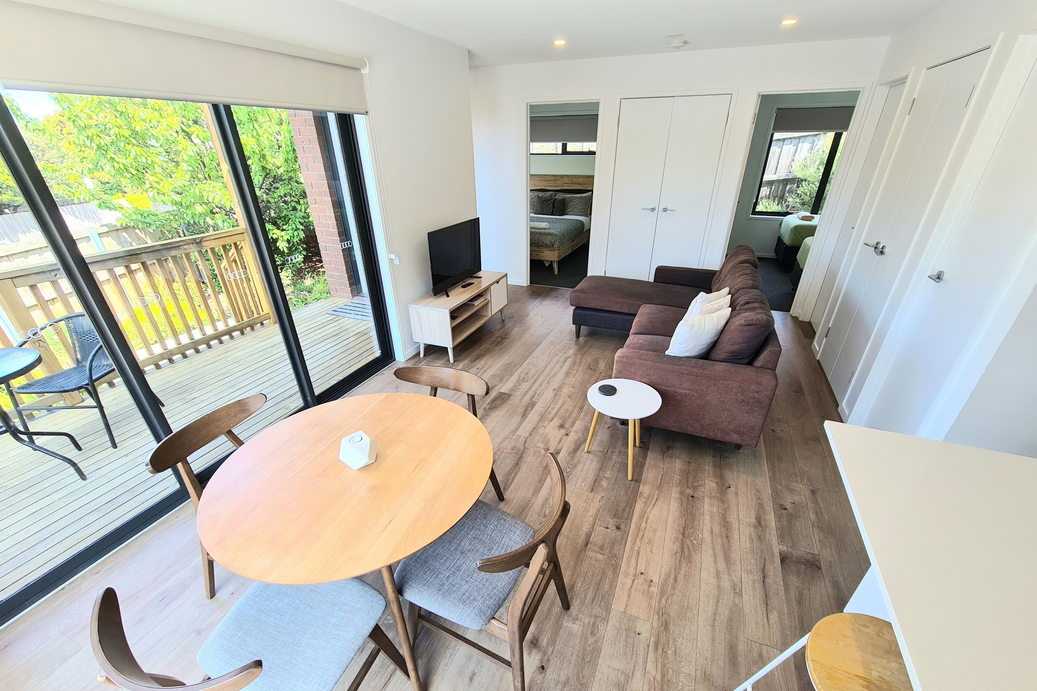 A modern living room with a wooden floor, a round dining table, a sofa, and a TV on a stand.