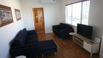 A living room with a dark blue sofa set, a small white table, a TV on a wooden stand, and a door leading to another room.