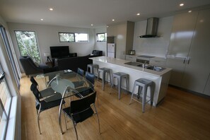 Une cuisine moderne dotée d’un îlot central, de tabourets de bar, d’une table à manger avec des chaises et d’une grande fenêtre qui laisse entrer la lumière naturelle.