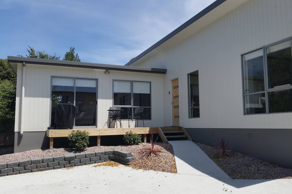 Une maison moderne à deux étages, dotée d’une terrasse, de grandes fenêtres et d’un petit jardin.