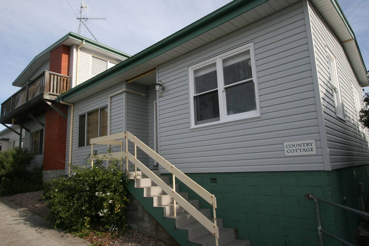 Une maison à deux étages, à l’extérieur peint en vert, avec une enseigne indiquant « Country Cottage ».