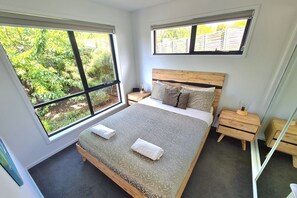 Une chambre à coucher avec un grand lit, deux tables de chevet et deux fenêtres donnant sur un paysage verdoyant.