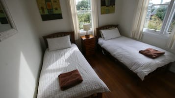 A room with two single beds, a nightstand, a window with curtains, and artwork on the walls.