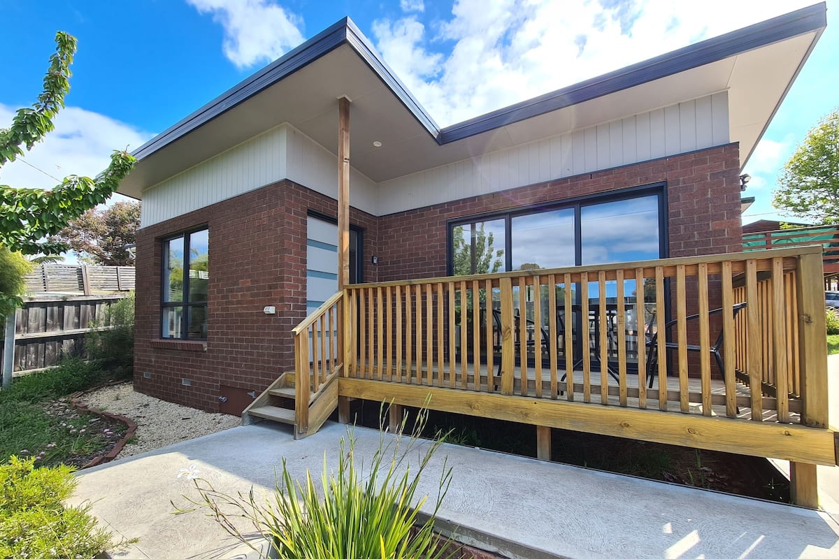 Une maison moderne à deux étages, avec une façade en briques, de grandes fenêtres et une terrasse en bois.