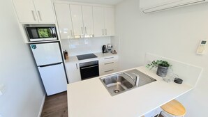 Eine moderne Küche mit weißen Schränken, einer eingebauten Mikrowelle, einem Kühlschrank, einem Geschirrspüler und einem Waschbecken mit Armatur aus Edelstahl.