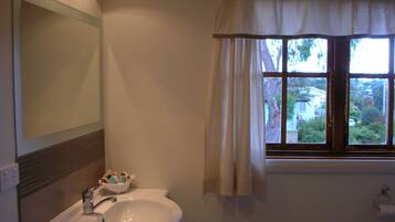 A bathroom with a sink, mirror, window with curtains, and a view of the outside.
