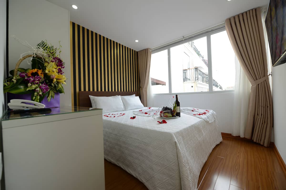Ein Hotelzimmer mit einem Bett, einem Schreibtisch mit Telefon, einem Fenster mit Vorhängen und einer Wand mit vertikalem Streifenmuster.