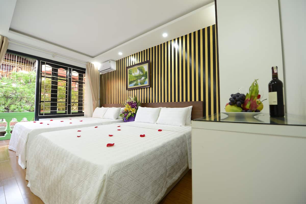Ein Hotelzimmer mit zwei Betten, einem großen Fenster, einem Wandbild und einer Obstschale mit einer Flasche auf dem Nachttisch.