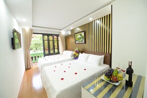 A hotel room with two beds, a dining table with a bottle of wine, and a view of greenery outside. - Hanoi Golden Hostel (Hanoi)