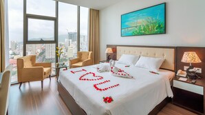 Habitación de hotel con una cama grande, dos sillas, una mesita de noche y vistas a la ciudad.