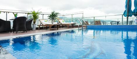 Un área de piscina en la azotea con sillas de descanso, una pequeña mesa y plantas en macetas.