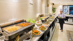 Un bufé con diversos platos, un cocinero y una cocina moderna al fondo.