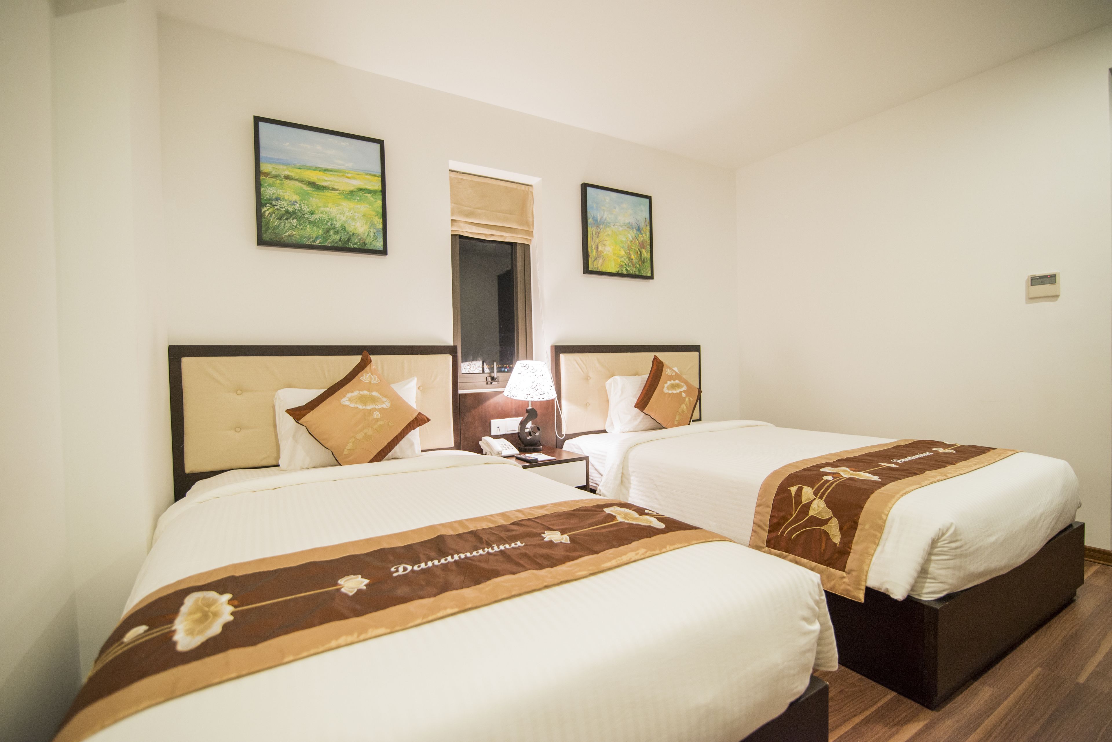 A hotel room with two beds, each with a brown floral bedspread, a nightstand with a lamp, and a mirror on the wall.