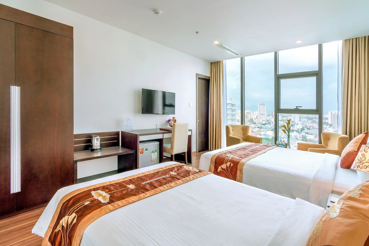 Quarto de hotel com duas camas, uma escrivaninha, uma televisão e vista para a cidade.