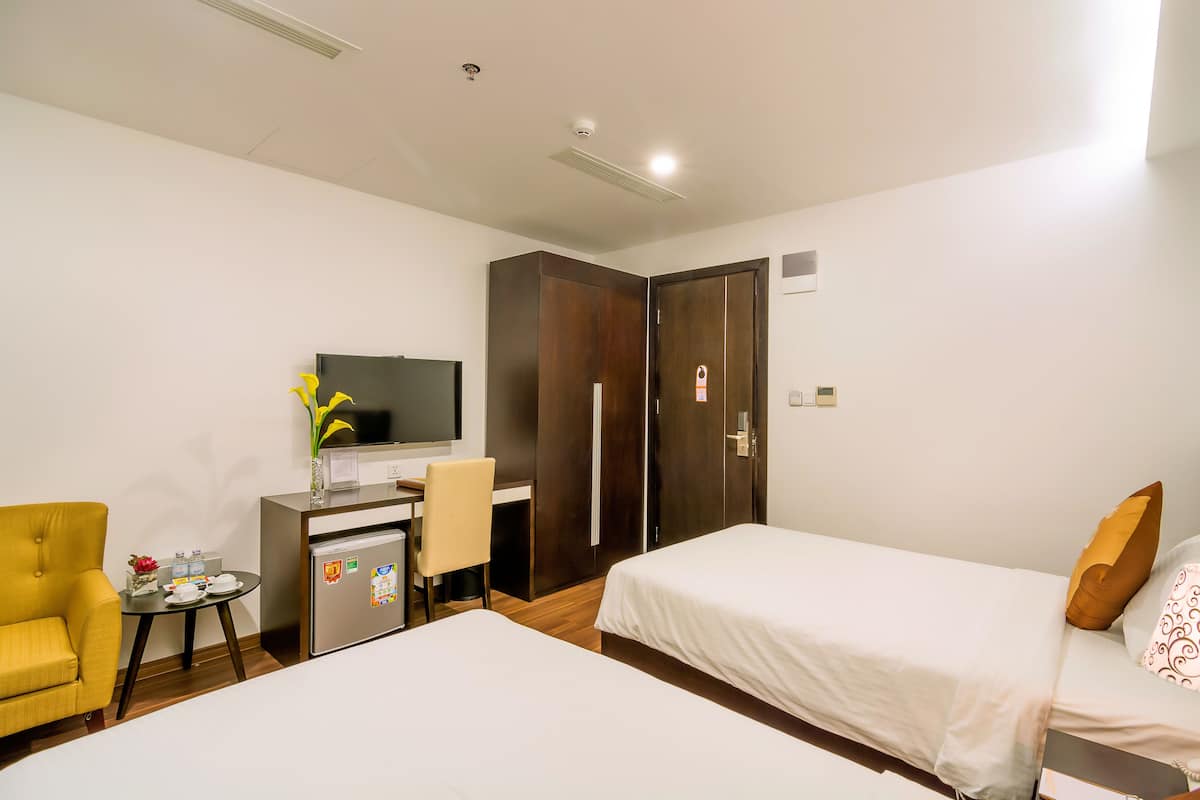 Quarto de hotel com duas camas, uma escrivaninha com cadeira, televisão e uma pequena mesa com um vaso de flores.