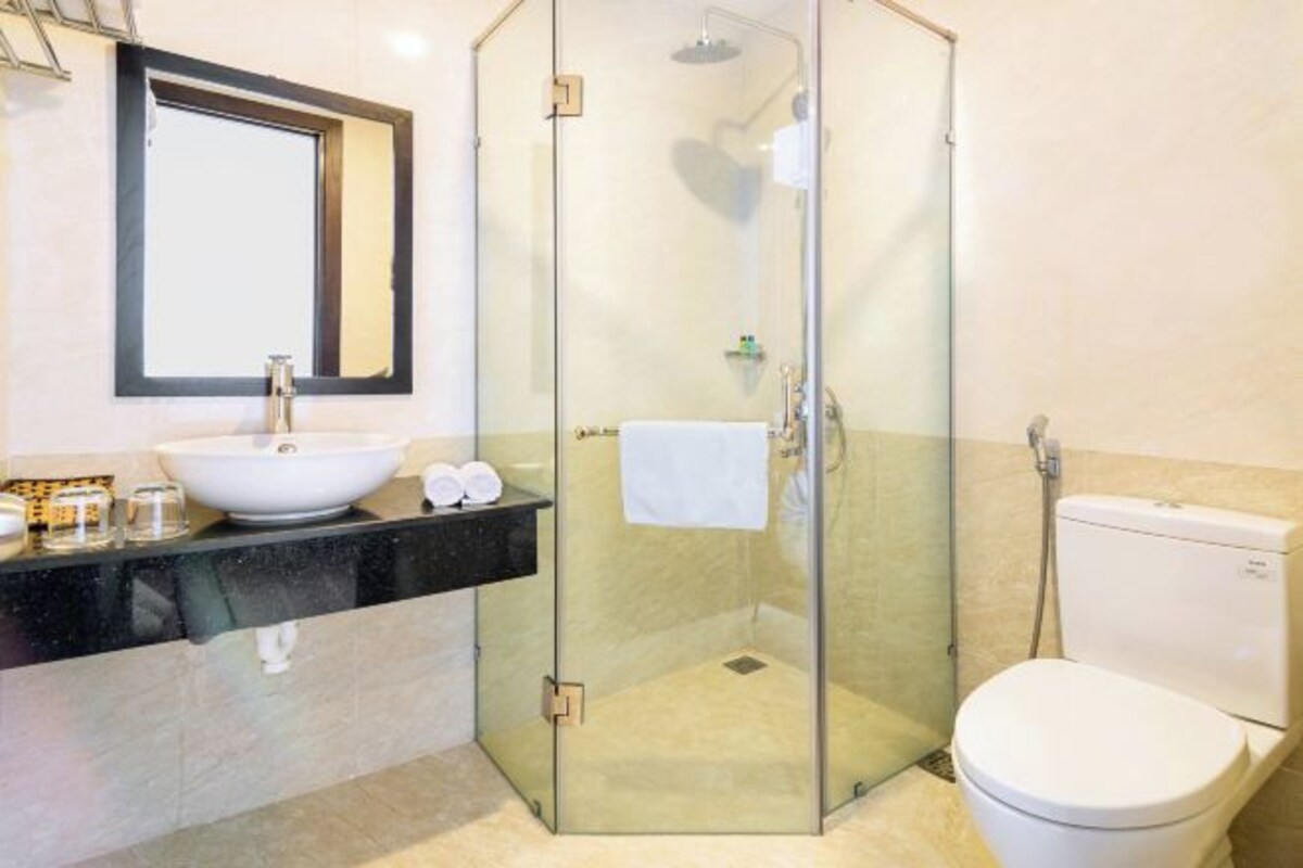 A modern bathroom with a glass-enclosed shower, a white sink with a large mirror, and a white toilet.