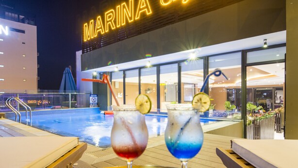Un bar junto a la piscina con dos bebidas, una piscina y un edificio con el letrero 'MARINA'.