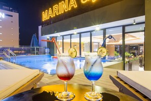 A poolside bar with two drinks, a pool, and a building with a 'MARINA' sign. - Dana Marina Hotel (Da Nang)